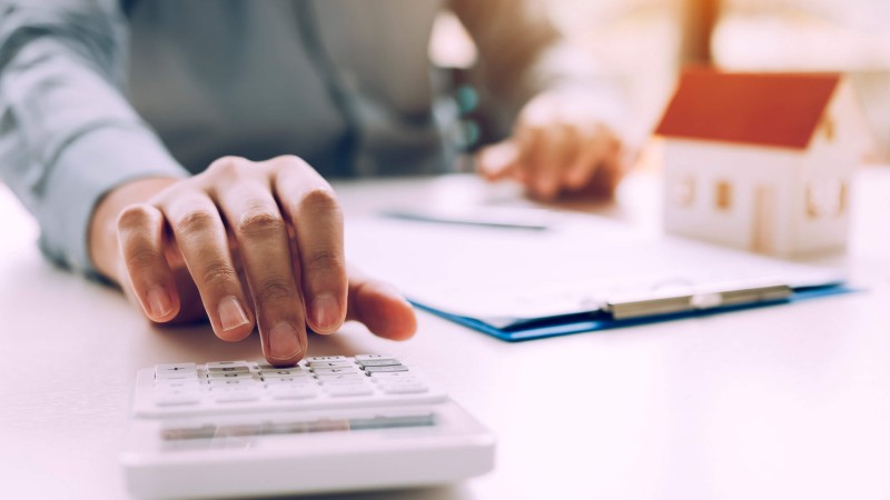 Personne assise à un bureau, effectuant des calculs sur une calculatrice - Multi-Prêts Hypothèques
